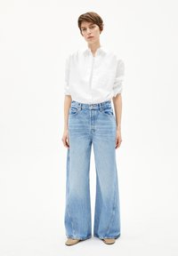 Himmelblaue weit geschnittene Jeans mit hoher Taille, kombiniert mit einem weißen Hemd mit Knöpfen. Weicher Denimstoff mit einem dezenten, ausgewaschenen Muster.