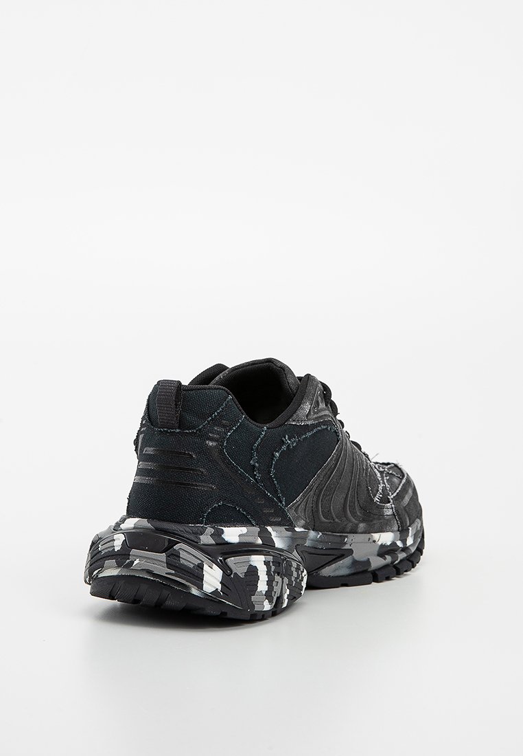 Des chaussures de sport noires présentent une tige en tissu texturé avec des accents courbés, une semelle à motif camouflage et un support de talon renforcé.