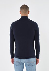 Cămașă turtleneck dintr-un material neted, de culoare bleumarin, cu mânecă lungă, ajustată pe corp, guler înalt și umeri fără cusături, asortată cu blugi de un albastru deschis.