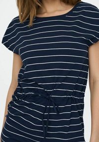 Marineblaue T-Shirt mit weißen horizontalen Streifen, Rundhalsausschnitt und kurzen Ärmeln. Verfügt über einen Kordelzug an der Taille für eine verstellbare Passform.