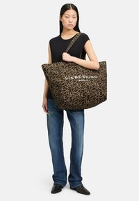 Torba tote w panterkę o przestronnym designie, wykonana z tkaniny, z wyraźnym logo i szerokim paskiem na ramię. Teksturowana powierzchnia.