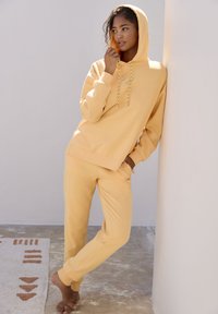 Gelbe Kapuzenjacke und passende Sweatpants aus weichem Material; mit einer verstellbaren Kapuze und lockerer Passform, die minimale Designdetails aufweisen.