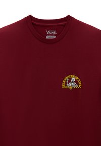 Camiseta de algodón burdeos con cuello redondo; presenta un logotipo gráfico de un esqueleto sosteniendo una patineta con acentos en amarillo y negro.
