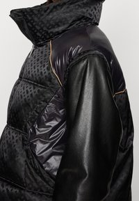 Czarna puchowa kurtka o błyszczącym wykończeniu, z pikowanymi sekcjami w wzory oraz skórzanymi rękawami. Posiada wysoki kołnierz i widoczny detal zamka błyskawicznego.