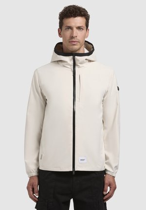 Cream-colored jacket with a black zipper and hood. Features elastic cuffs, a smooth texture, and a logo patch on the lower hem.