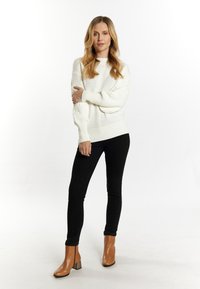 Weißer Strickpullover mit strukturiertem Muster, schwarze Skinny Jeans und braune Ankle Boots mit Blockabsatz. Schlichtes und modernes Design.
