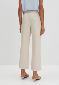 Pantalones de pierna ancha de un beige claro con un acabado texturizado, que cuentan con una cinturilla flexible y bolsillos traseros, complementados con sandalias sencillas.