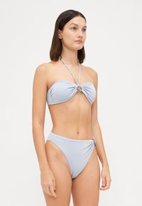 Világoskék bikini szett, melynek bandeau felsőrésze középen fémgyűrűvel rendelkezik, és magasan szabott alsó része oldalrészletel ellátott.
