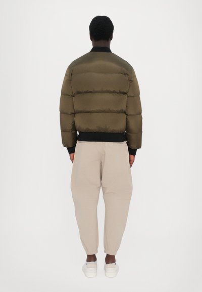 Veste en duvet olive verte avec design matelassé horizontal, col noir côtelé et poignets élastiques. Associée à un pantalon tapered beige clair.