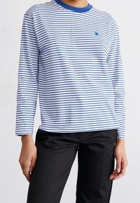 Långärmad randig skjorta med blå och vita horisontella ränder, en blå rundhalsad halsringning och en liten logotyp på bröstet.