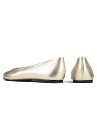 Bailarinas metálicas doradas con un acabado suave y brillante, punta redondeada y suela plana. Diseño minimalista, con bordes sin costuras y sin adornos visibles.