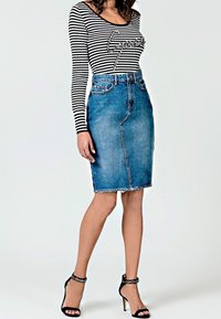 Falda lápiz de mezclilla con un lavado azul claro, presenta una costura en el frente y un dobladillo deshilachado, combinada con una blusa de manga larga a rayas en blanco y negro y tacones negros.