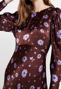 Brun satinklänning med puffärmar och en blommönster i lavendel och svart, med en åtsittande bodice och en flödande kjol.