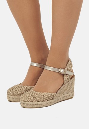 Cuñas de esparto beige con una correa metálica en el tobillo, que presentan una parte superior texturizada y una suela cuña envuelta en yute.