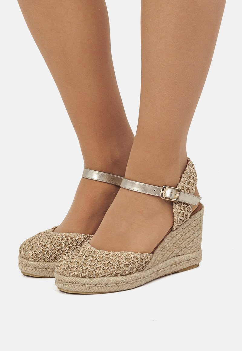 Cuñas de esparto beige con una correa metálica en el tobillo, que presentan una parte superior texturizada y una suela cuña envuelta en yute.