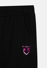 Schwarze Jogginghose mit einem elastischen Bund. Besitzt ein pinkes reflektierendes Logo mit Sternen und Herzen auf der linken Seitentasche. Weicher Stoff.