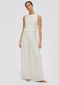 Crème wijde jumpsuit met een mouwloze top. Bevat een gladde stof, subtiele plooien en een relaxte pasvorm. Eenvoudig ontwerp zonder versieringen.