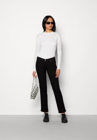 Top de manga larga blanco con textura acanalada, vaqueros ajustados negros, zapatos negros con cordones y un bolso a rayas en blanco y negro. Diseño simple y moderno.