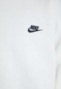 Balta džemperis ar mazu melnu Nike logotipu izšūti kreisajā krūtīs. Materiāls izskatās mīksts ar gludu tekstūru.