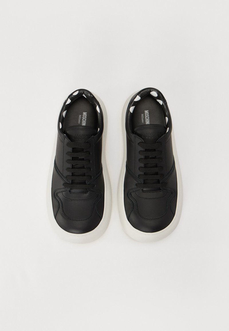 Zwarte leren sneakers met ronde neus, witte rubberen zolen en zwarte veters. Binnenin is er een stippenpatroon. Eenvoudige, minimalistische stijl.