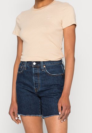 Kvinde iført en beige og hvid stribet kortærmet top stukket ned i høj taljede mørk denimshorts med rå kanter.