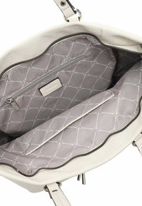 Binnenkant van een witte leren handtas met grijze stoffen voering die een geometrisch patroon vertoont, een ritsvak en een contrasterende zwarte rits.