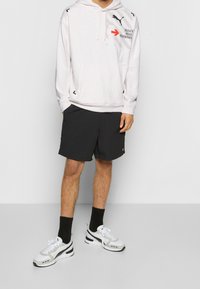 Světle šedá mikina s grafickým designem, černé šortky, černé ponožky a bílé tenisky se šedými akcenty, které vytvářejí sportovní a ležérní vzhled.