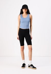 Plava rebrasta majica bez rukava, crne uske biciklističke šortse, crna kapa i crne tenisice s bijelim prugama. Glatka tkanina, ležeran sportski stil.