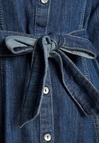 Close-up of a tied denim fabric belt on a buttoned dark blue denim garment with visible stitching details.