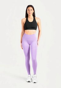 Sort sports-bh, tætsiddende, med rund halsudskæring. Lyse lilla leggings med høj talje og glat tekstur. Hvide sportssko med detaljer.