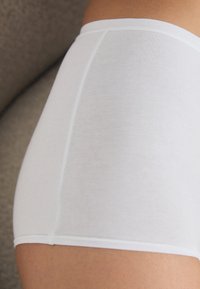 Hvit høyhals undertøy laget av glatt stoff. Har en ren finish ved midjen og benåpningene, med et sømløst design.