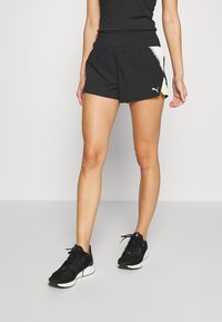 Black athletic shorts with a wide elastic waistband, featuring a contrasting side panel in light colors. Paired with black sports shoes.