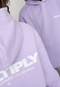 Felpe color lavanda con il testo bianco "MULTIPLY APPAREL CLUB 2024". Presenta un cappuccio con coulisse e una texture di tessuto morbido e liscio.
