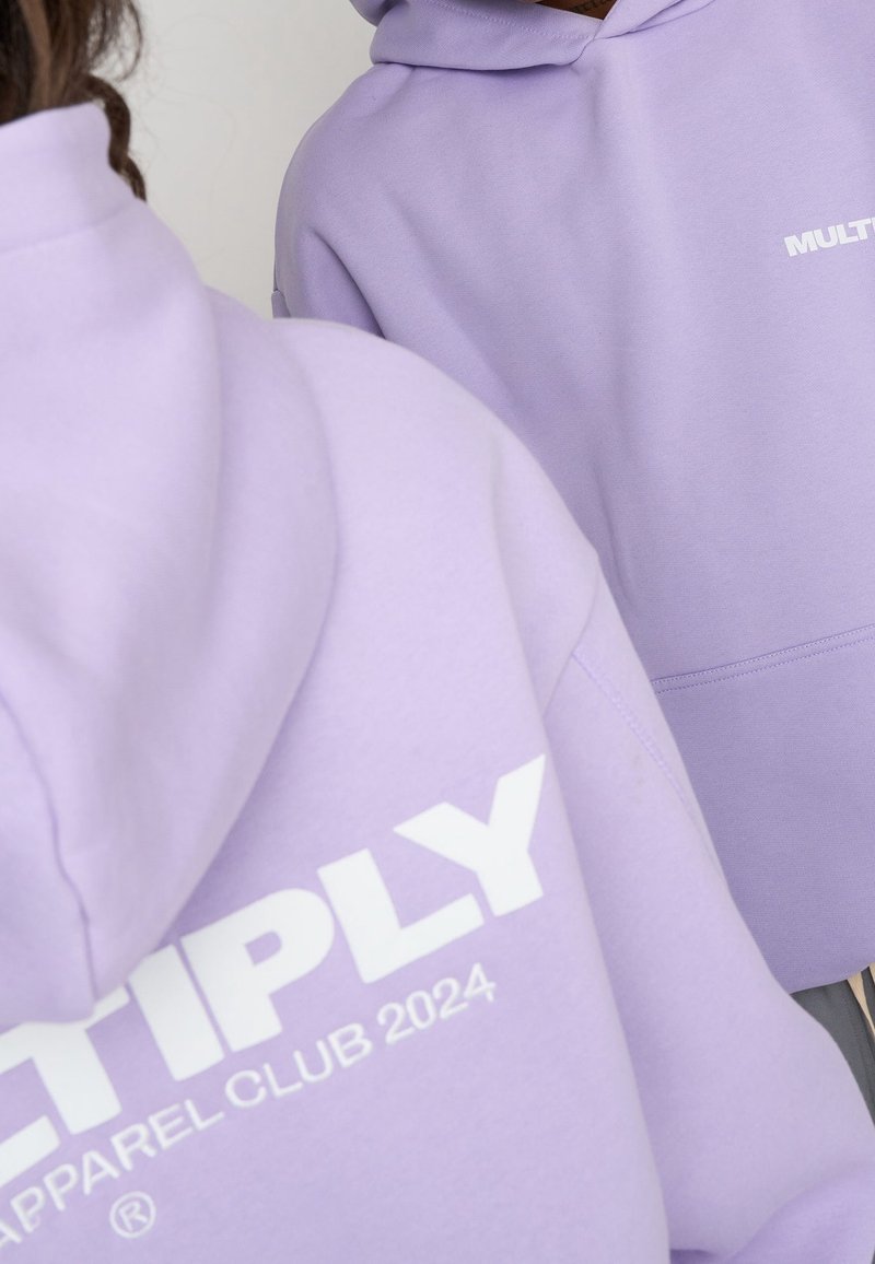 Felpe color lavanda con il testo bianco "MULTIPLY APPAREL CLUB 2024". Presenta un cappuccio con coulisse e una texture di tessuto morbido e liscio.