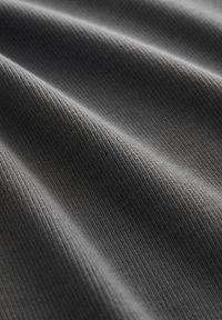 Tissu gris foncé texturé avec un motif côtelé, présentant des plis doux et ondulés. Le matériau semble lisse et léger.