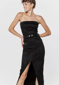 Czarna sukienka bez ramiączek z dopasowanym gorsetem i wysokim rozcięciem. Posiada paskiem w talii z srebrnymi guzikami oraz gładką, teksturowaną tkaninę.