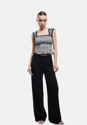 Svart- och vitt rutigt crop top med volanger längs kanterna, kompletterat med lösa svarta byxor. Har enkla hoop örhängen och öppna sandaler.