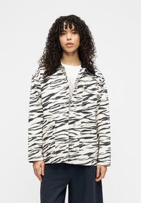 Ζακέτα με μοτίβο ζέβρας σε λευκό και μαύρο ύφασμα, με γιακά, μπροστινά κουμπιά, δύο μπροστινές τσέπες και ελαφρώς φαρδιά γραμμή.