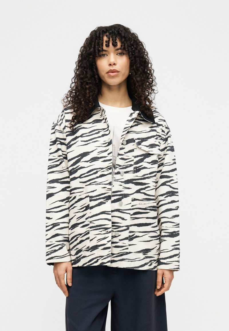 Ζακέτα με μοτίβο ζέβρας σε λευκό και μαύρο ύφασμα, με γιακά, μπροστινά κουμπιά, δύο μπροστινές τσέπες και ελαφρώς φαρδιά γραμμή.