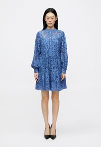 Μπλε δαντελένιο φόρεμα με ψηλό λαιμό, μακριά φουσκωτά μανίκια και ρέουσα βάση. Το υλικό έχει λουλουδάτο μοτίβο με διαφανείς λεπτομέρειες.