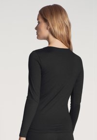 Zwarte langesleeve top van zachte stof, met een ronde halslijn en een getailleerd ontwerp, zonder zichtbare patronen of hardwaredetails.