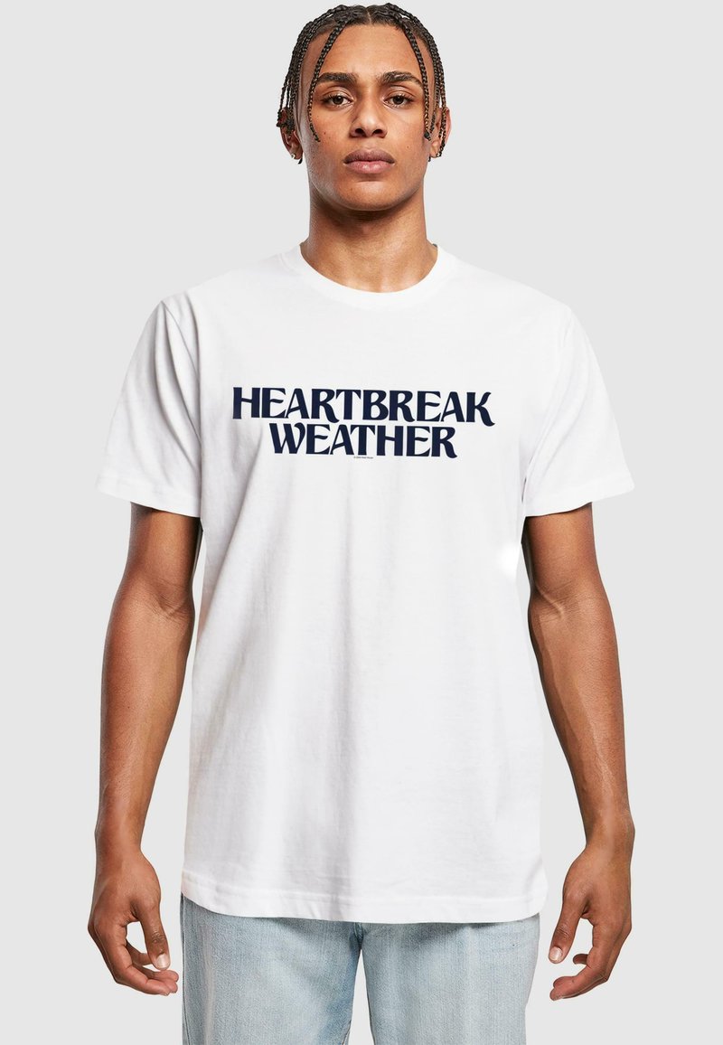 Hvit bomullst-skjorte med mørk marineblå tekst "HEARTBREAK WEATHER" i en fet, moderne skrifttype. Korte ermer og rund hals.