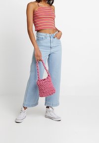 Bolso de mano tejido en color rosa con un asa retorcida, combinado con una blusa corta a rayas y unos jeans de tiro alto en azul claro. Zapatillas blancas completan el conjunto.