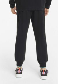 Svart joggebukse med elastiske mansjetter og strikket midje, paired med flerfargede sneakers som har en fremtredende hæltab og logodetaljer.