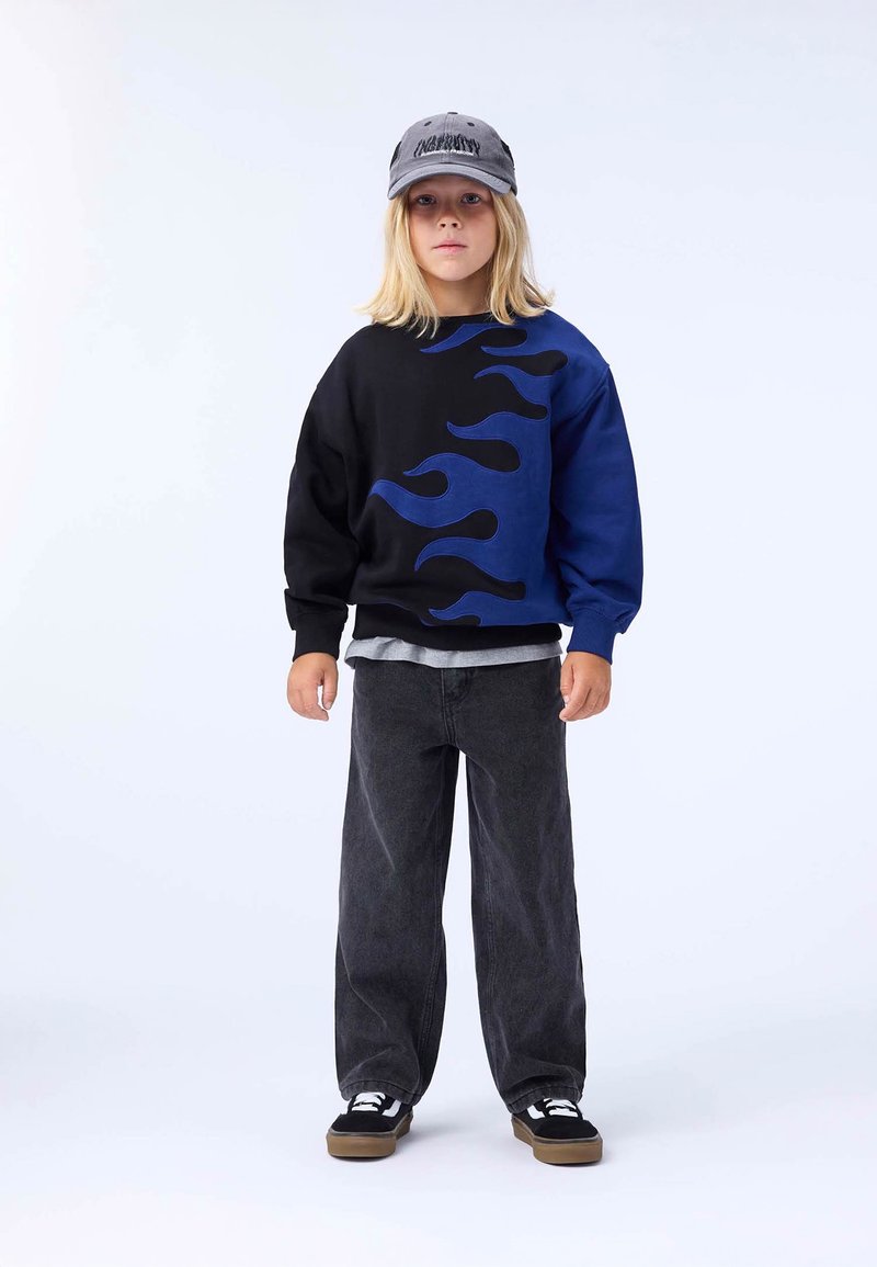 Svart och blå tröja med eldflammor, kombinerad med grå T-shirt, svarta vida jeans och svarta sneakers med vita detaljer.