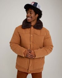 Bruine donzen jas met een faux bontkraag, drukknopen en geribbelde manchetten. Draagt een mesh-rugdeksel pet met een kleurrijke patch.