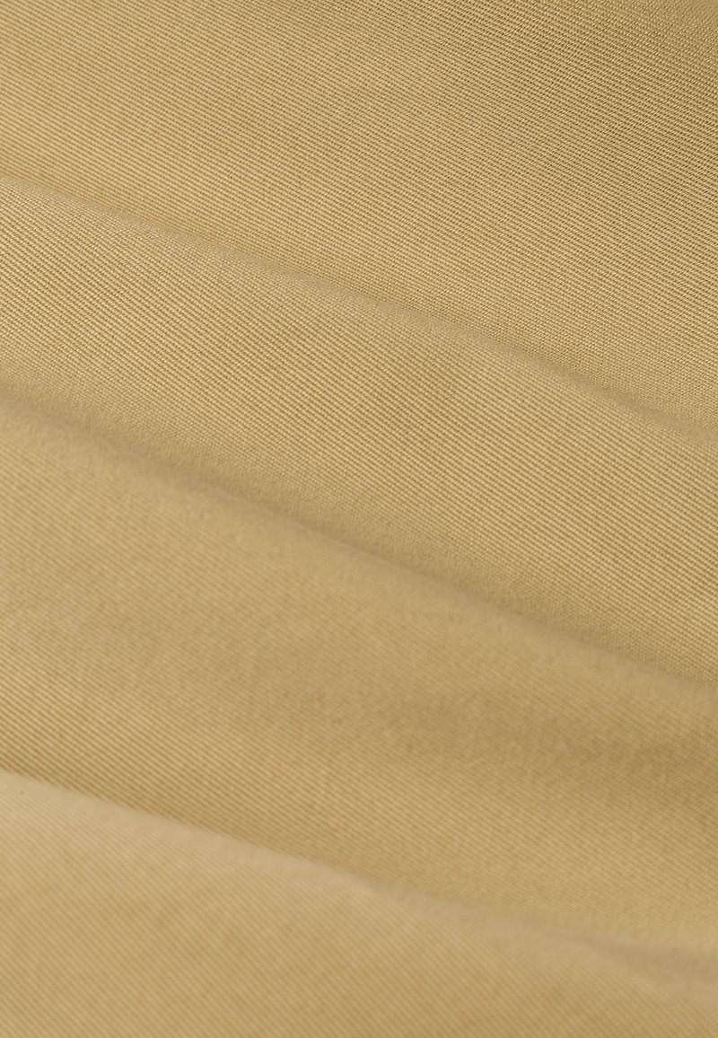 Beige Stoff mit einer weichen, strukturierten Oberfläche, die diagonale Falten und ein subtil geripptes Muster aufweist, welches Tiefe und visuelles Interesse schafft.