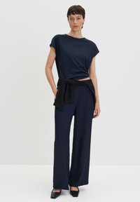 Top navy a maniche corte abbinato a pantaloni larghi a vita alta navy. Un maglione nero è legato in vita. Tessuto strutturato, gamba ampia.