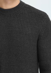 Mørkegrå strikket sweater med et struktureret mønster, ribbet rund halsudskæring og lange ærmer. Materialet ser blødt og varmt ud.