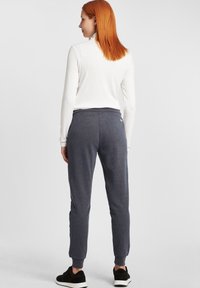 Grå joggerbyxor med elastisk midja och avsmalnande ben, tillverkade av ett mjukt, texturerat tyg. Bärs med en åtsittande vit topp och svarta sneakers.